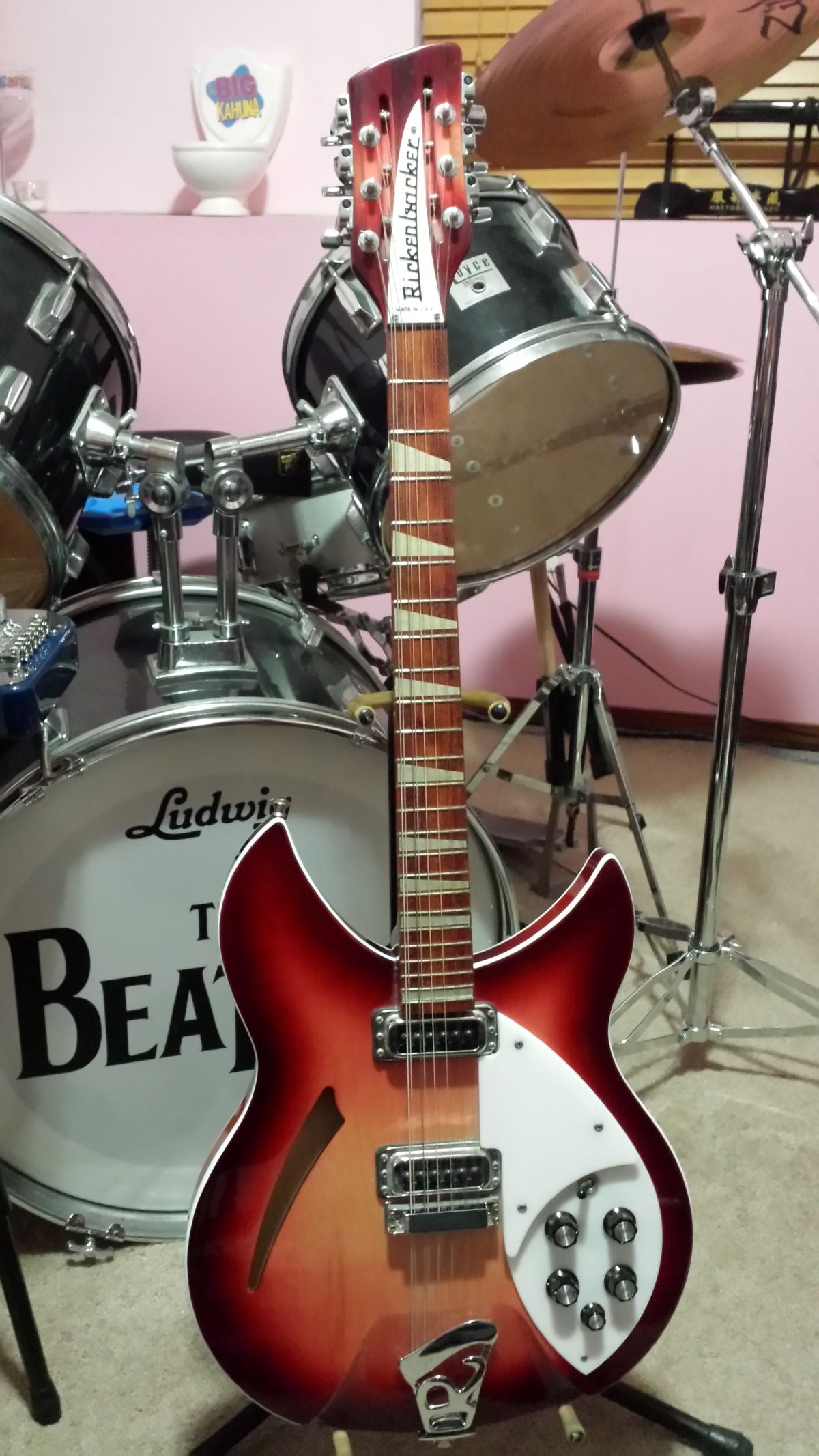 Electric guitar with a unique neck design in front of a drum set.